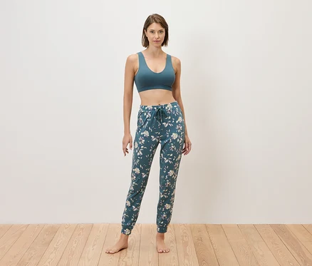 Femme debout pieds nus devant un mur portant un soutien-gorge de sport bleu et un pantalon de jogging bleu à fleurs.
