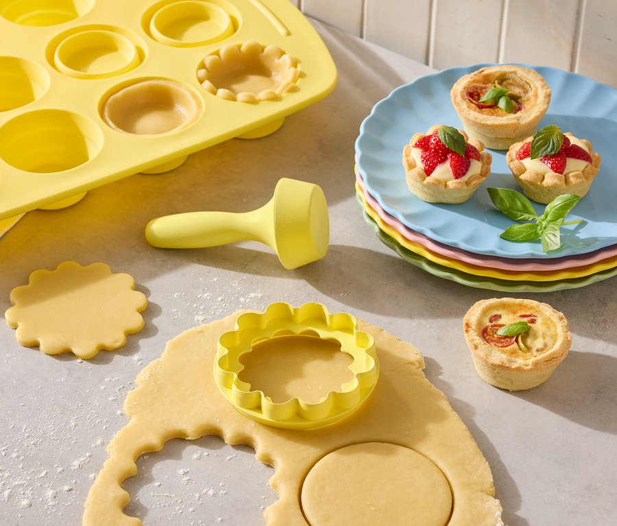 Moule à tartelettes jaune avec emporte-pièces et tartelettes cuites sur des assiettes colorées.