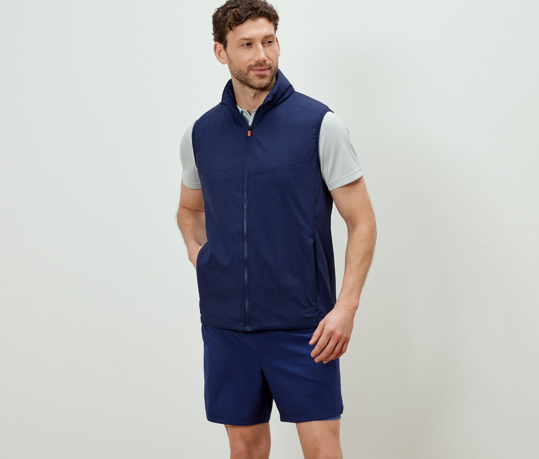 Un homme portant une veste fonctionnelle « packable » bleu marine et un short.