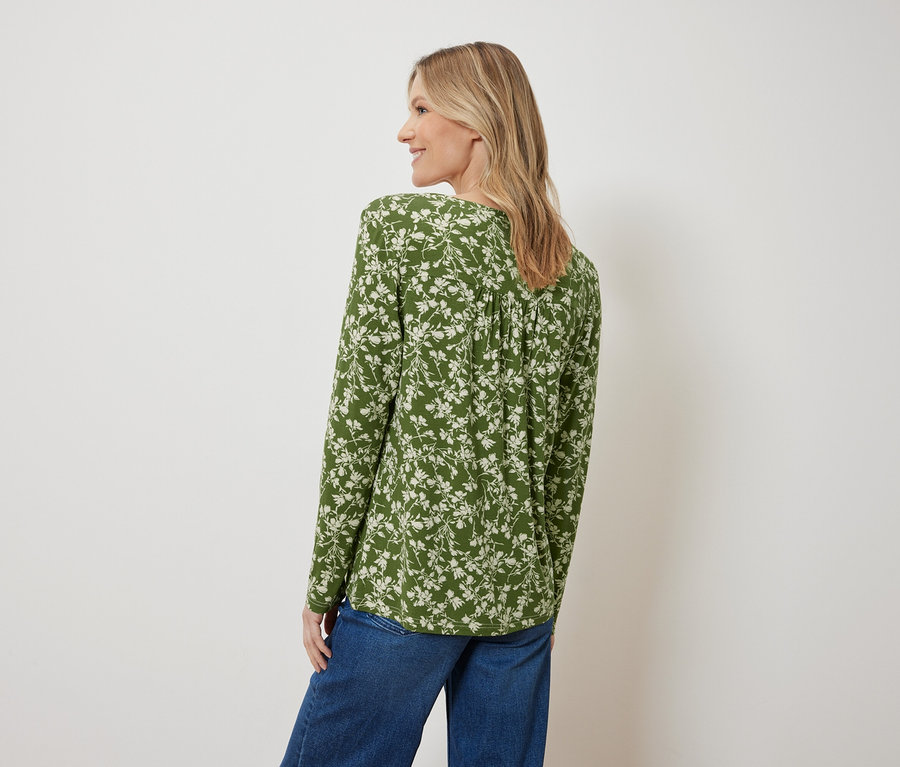 Vue arrière d'une femme blonde portant un chemisier vert à fleurs et un jean bleu.