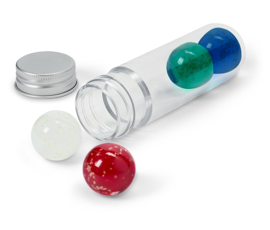 Un tube transparent est posé sur le côté avec une bille bleue et une bille verte à l'intérieur, un couvercle argenté à côté et une bille blanche et une bille rouge à l'extérieur.