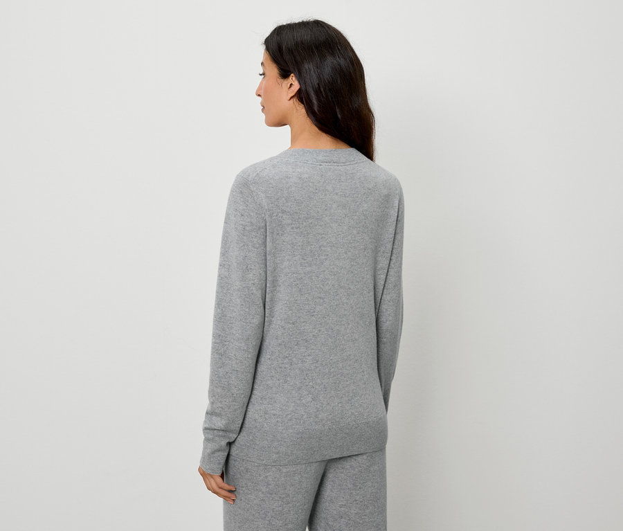 Vue de dos d'une femme aux cheveux foncés portant un pull et un pantalon gris.