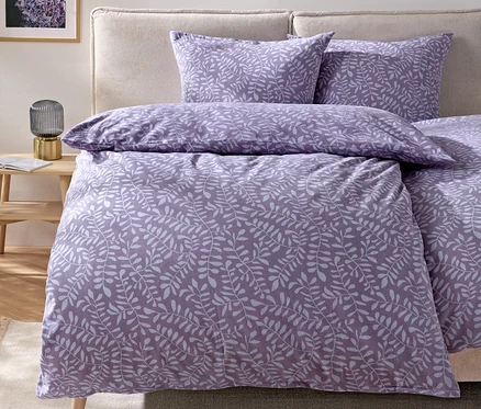 Linge de lit à motif de feuilles violettes sur un lit avec une tête de lit beige.