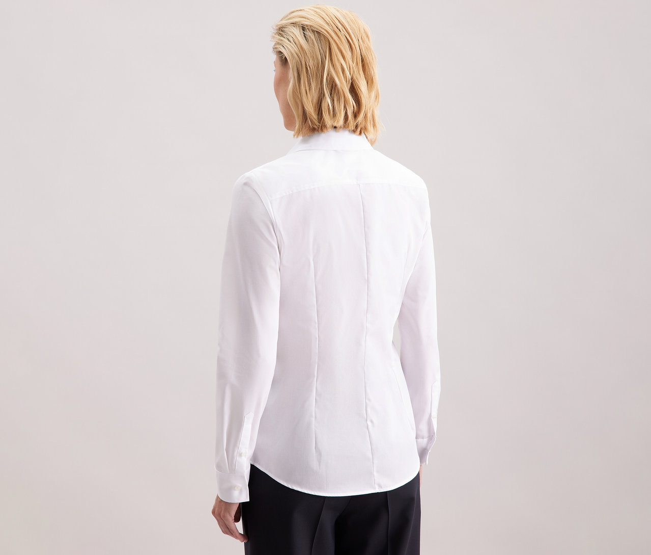 Vue arrière d'une femme blonde aux cheveux mi-longs portant un chemisier blanc Slim Fit non iron Seidensticker.