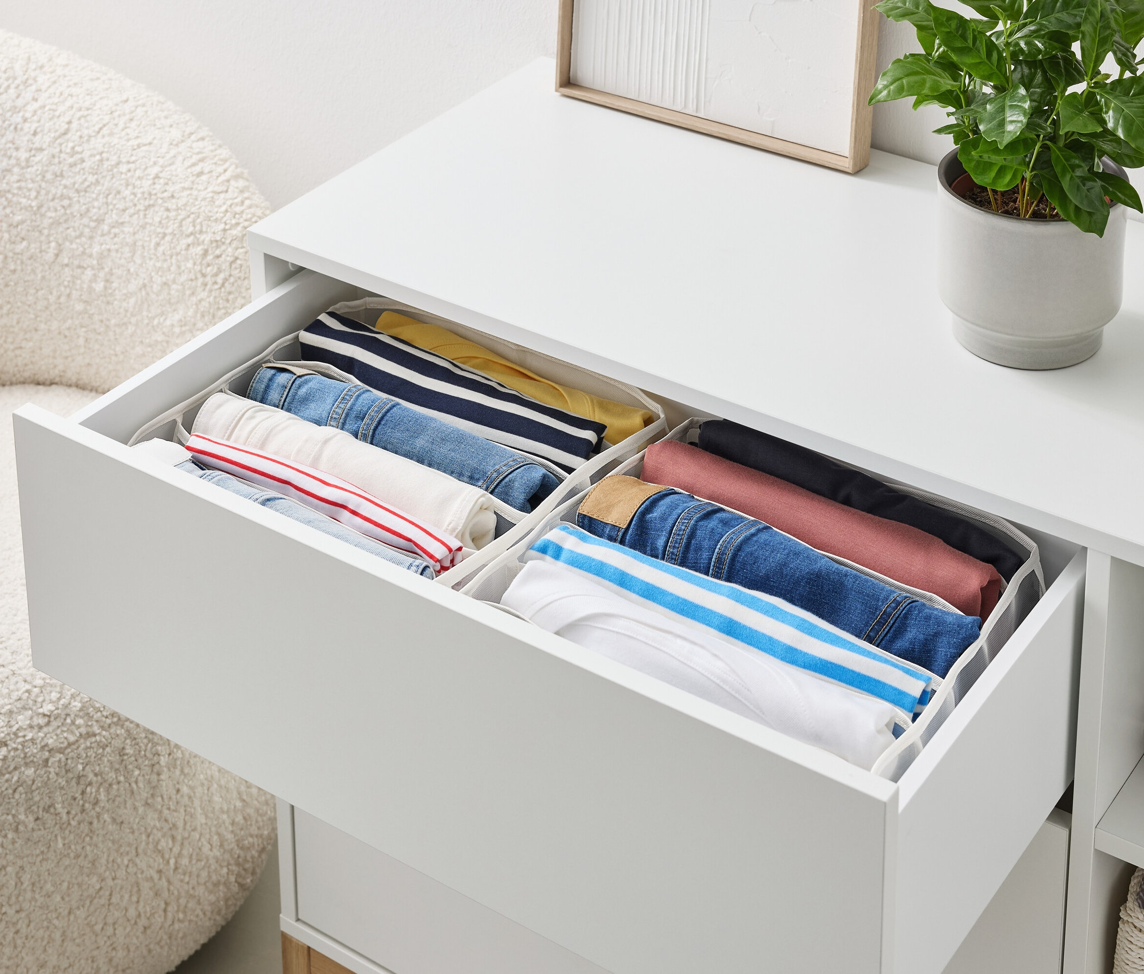 Un tiroir ouvert d'une commode blanche contient des vêtements soigneusement pliés dans des organiseurs.
