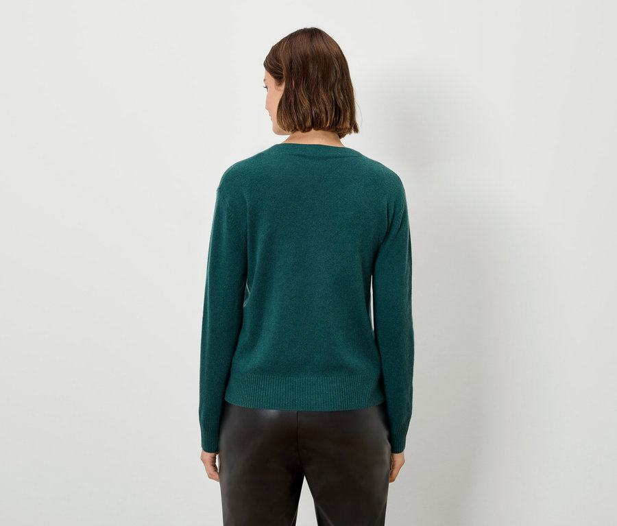 Une femme vue de dos, portant un pull vert et un pantalon noir.