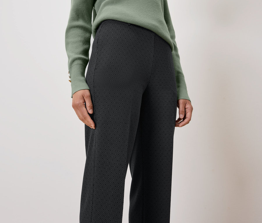 Une femme porte un pull vert et un pantalon noir à motifs.