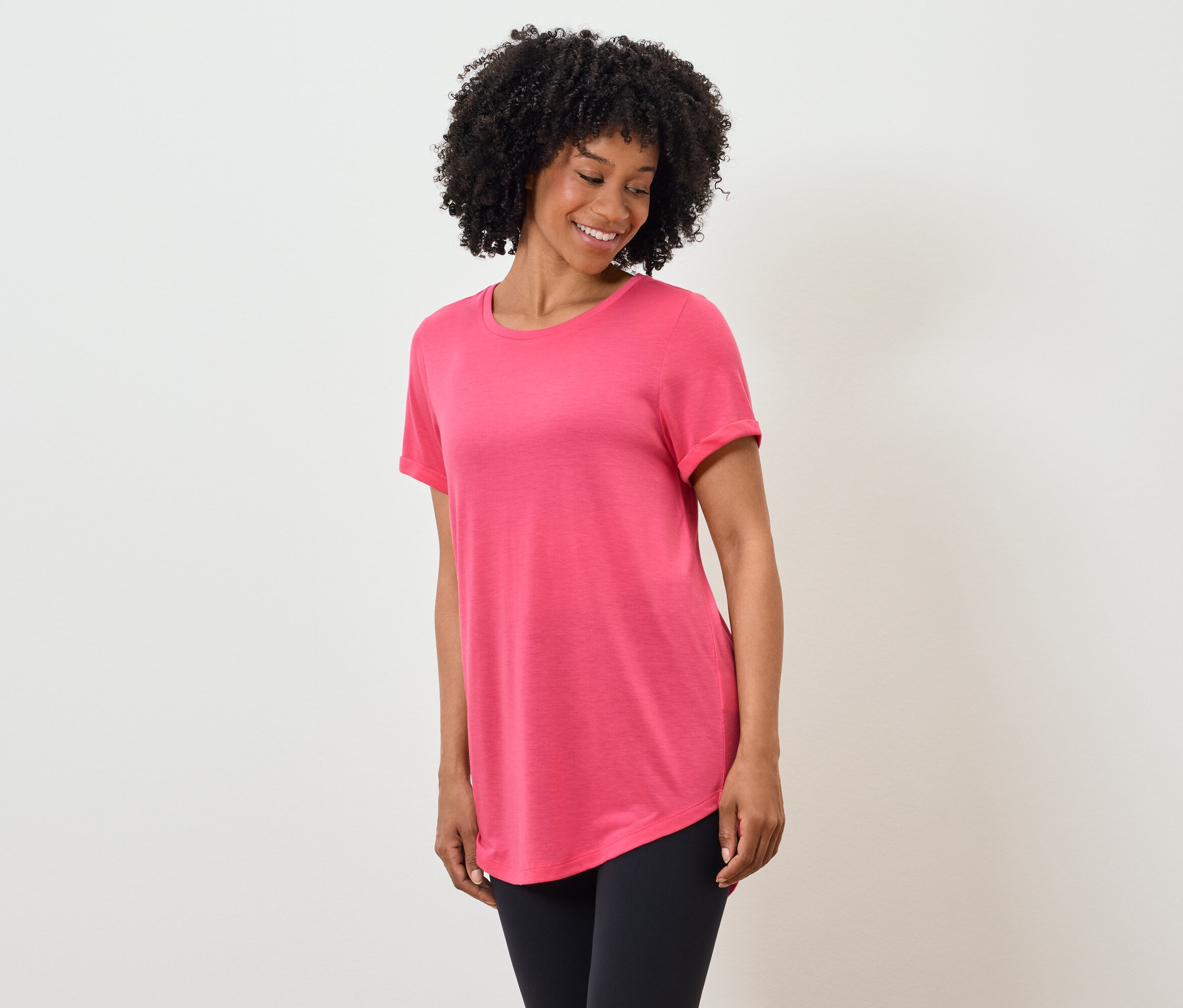 Une femme afro-américaine sourit et porte un t-shirt rose et un legging noir.