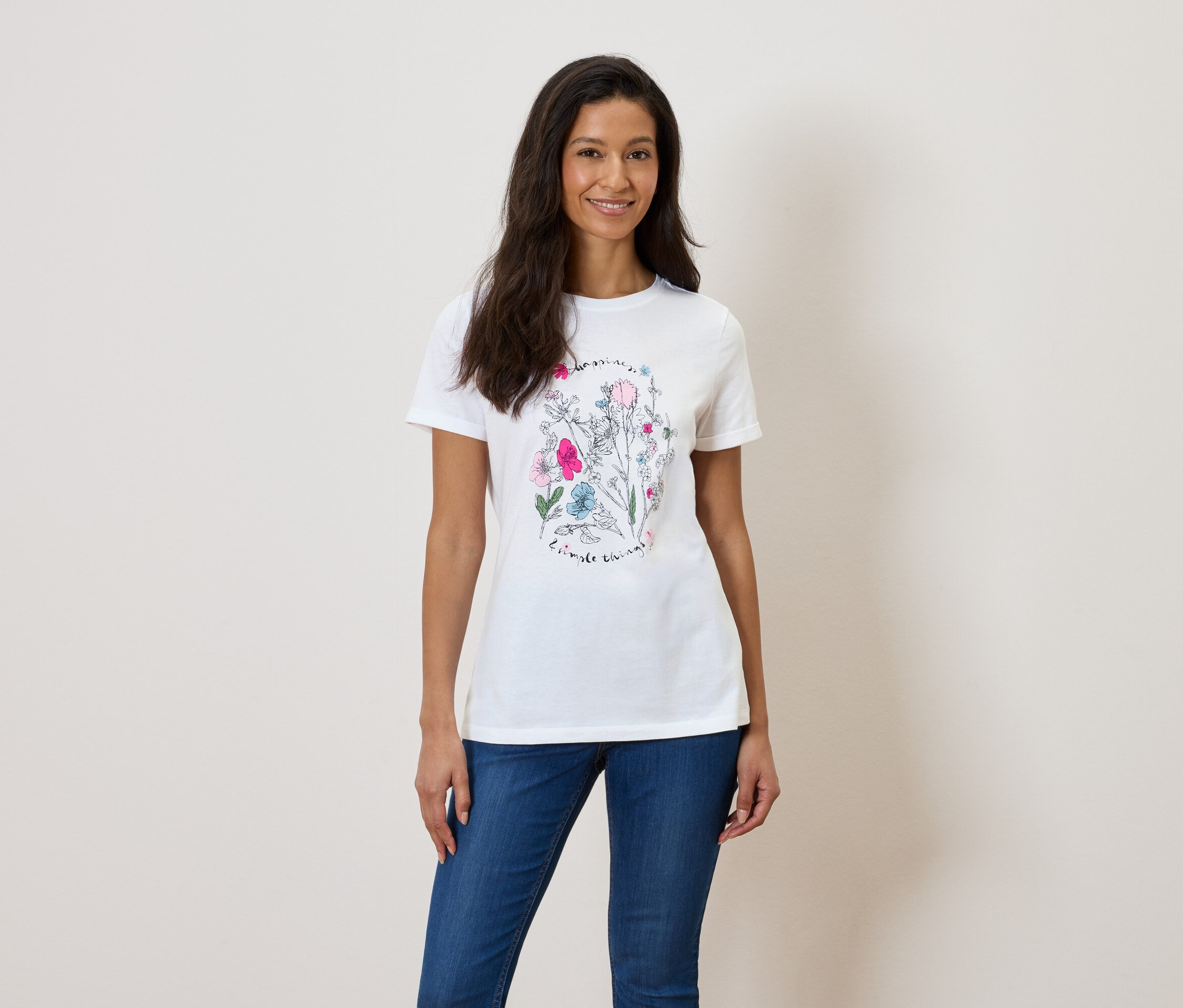 Une femme porte un t-shirt blanc avec un imprimé floral et un jean bleu.