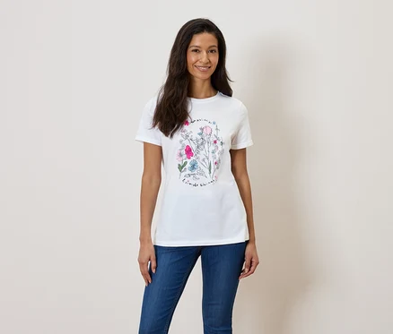 Une femme porte un t-shirt blanc avec un imprimé floral et un jean bleu.