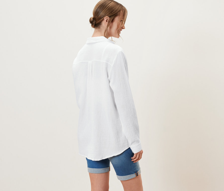 Une femme porte un chemisier en mousseline, blanc, et un short en jean.