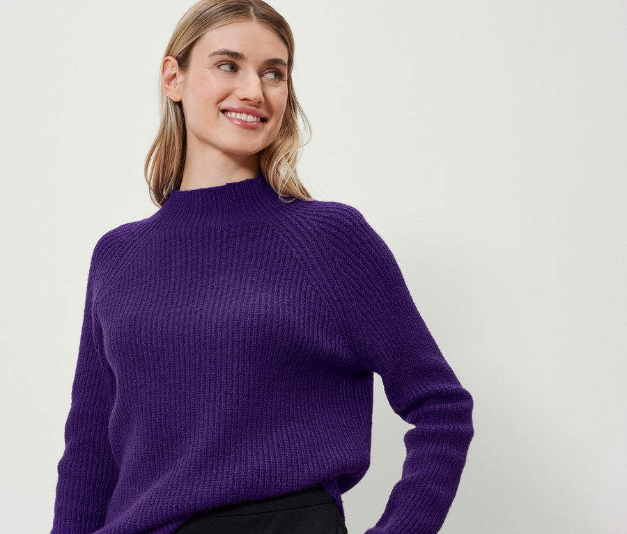 Une femme sourit et porte un pull violet.