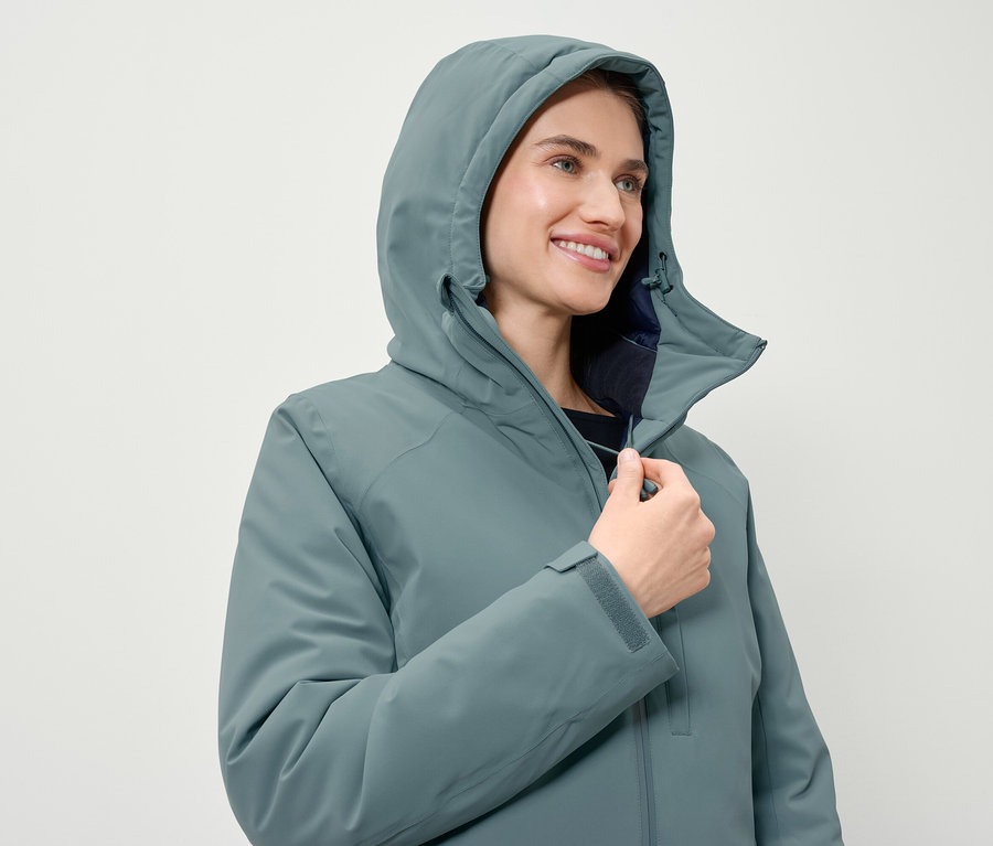 Femme fermant une veste bleu-vert à capuche.