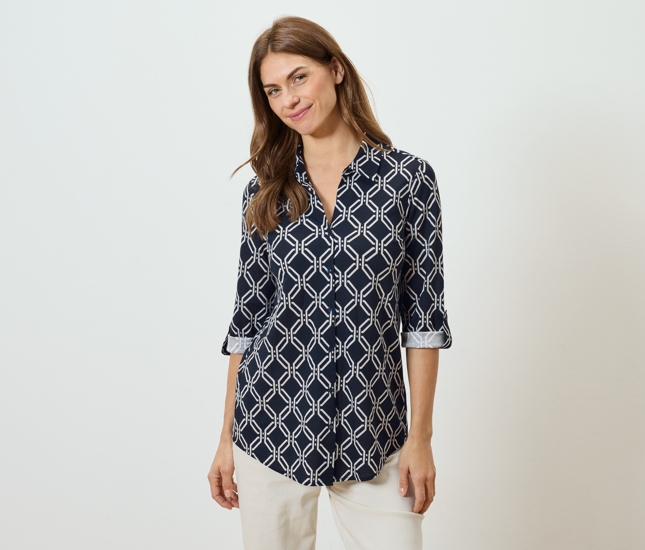 Femme portant un chemisier bleu marine à motifs géométriques blancs et un pantalon beige.