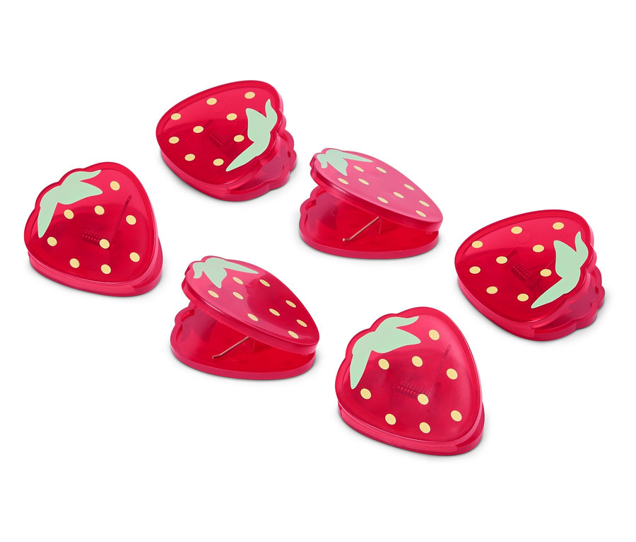Six pinces rouges en forme de fraise sont posées sur une surface blanche.