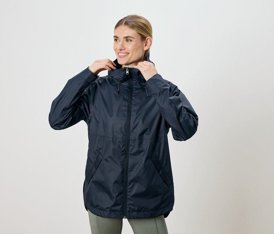 Femme ajustant une veste à capuche bleu marine et souriant.