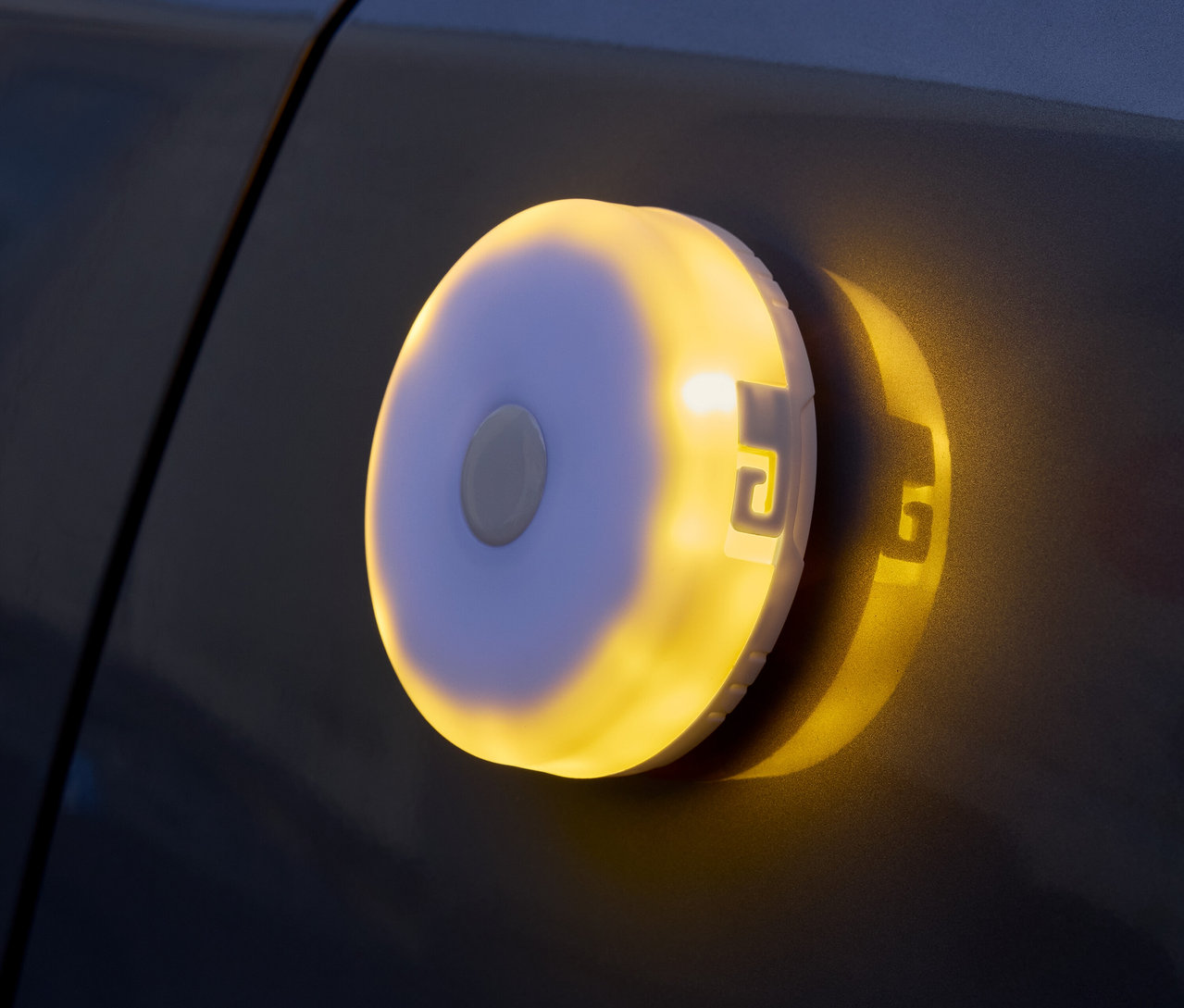 Une lampe ronde à piles émettant une lumière jaune est fixée sur une surface sombre.