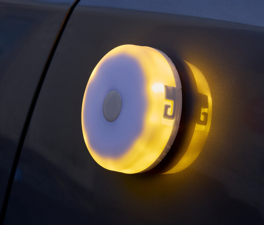 Une lampe ronde à piles émettant une lumière jaune est fixée sur une surface sombre.