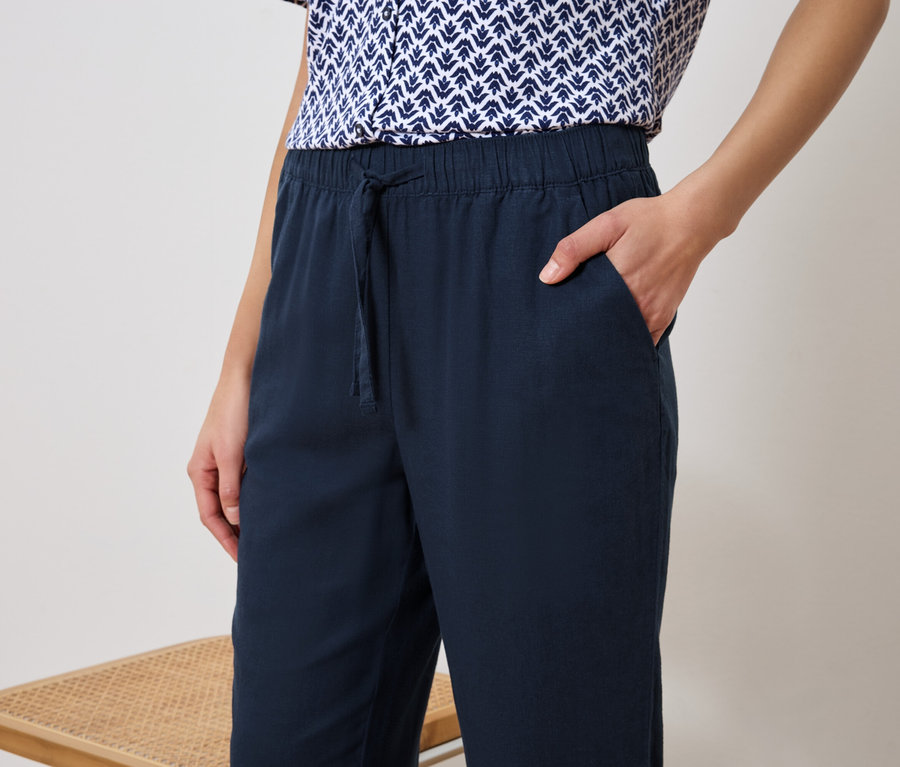 Femme portant un pantalon bleu marine et un haut à motifs bleu et blanc, la main dans la poche.