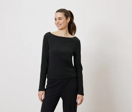 Femme souriante portant un haut noir à manches longues et un pantalon noir, les cheveux attachés en queue de cheval.
