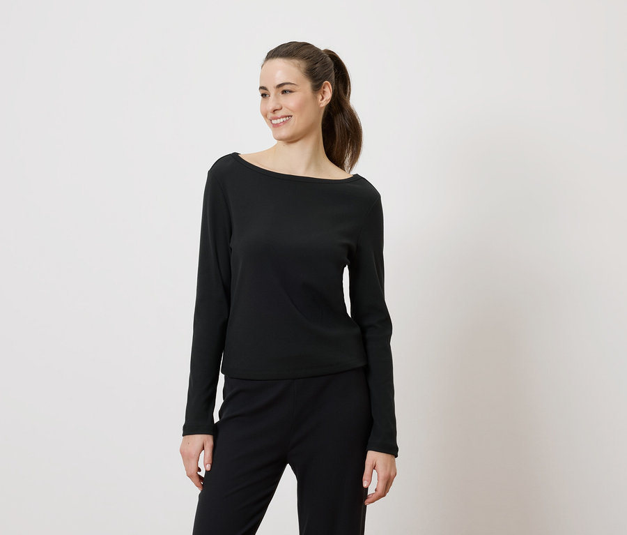 Femme souriante portant un haut noir à manches longues et un pantalon noir, les cheveux attachés en queue de cheval.