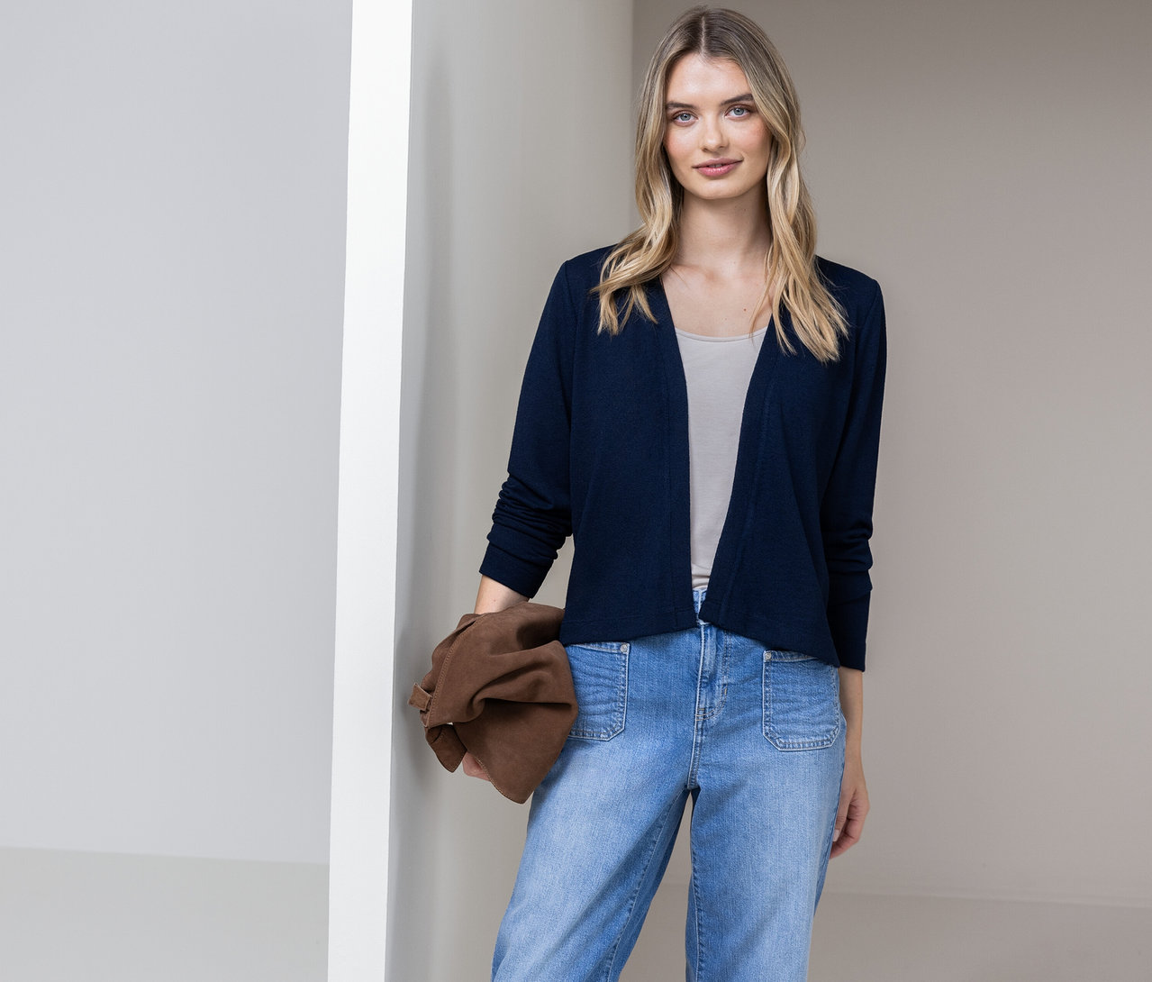 Femme portant un cardigan Street One bleu, un jean et tenant un sac marron devant un mur.