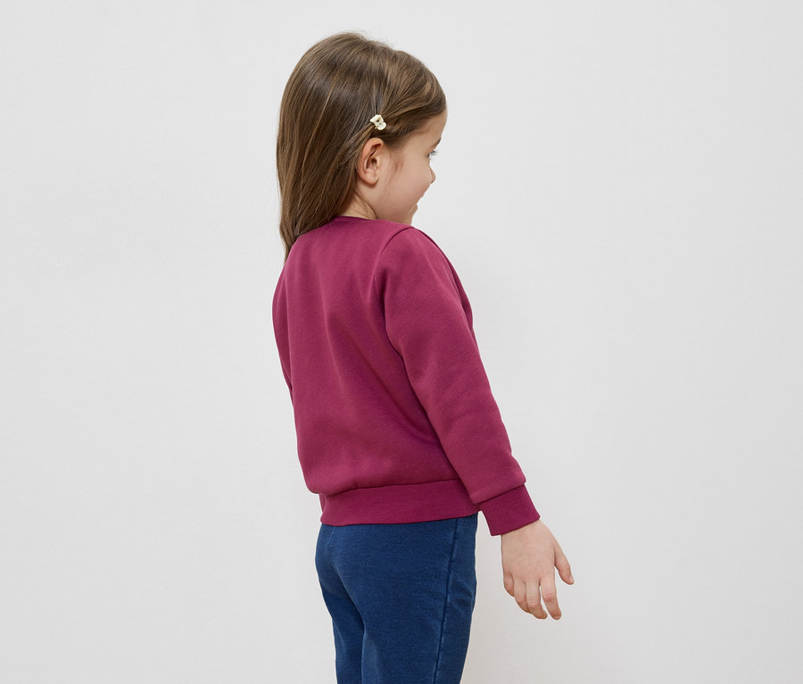 Fillette portant une barrette à cheveux, un pull bordeaux et un jean bleu, vue de dos.