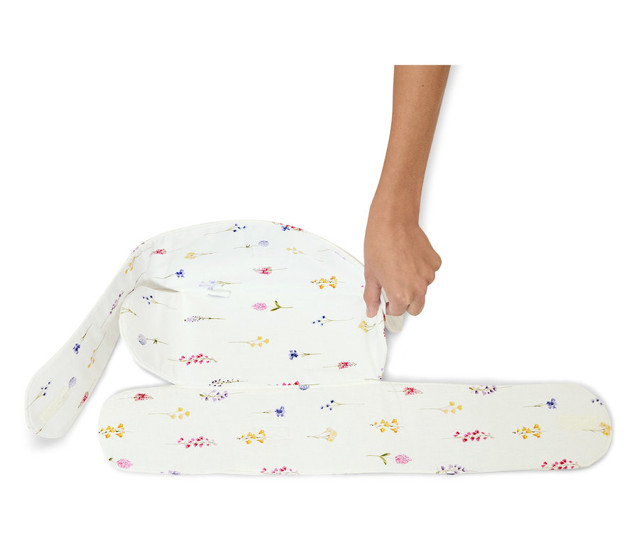 Une main plie un coussin d'allaitement blanc à motifs floraux.