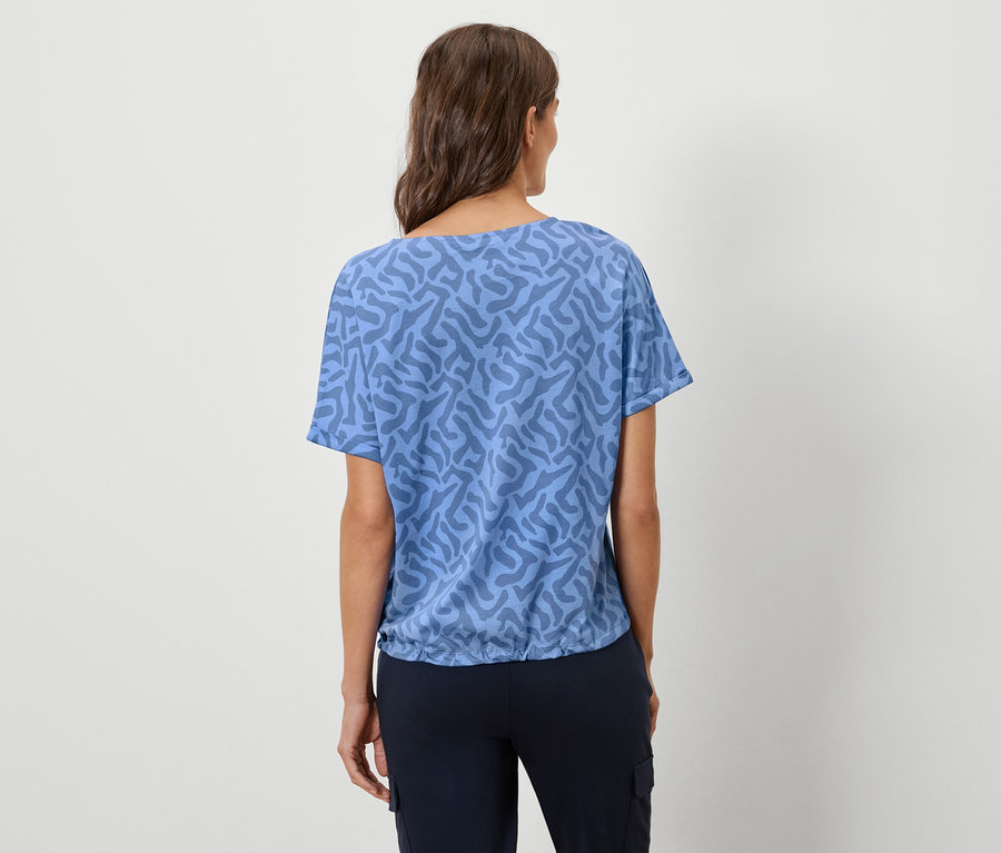Vue de dos d'une femme aux cheveux bruns portant un t-shirt bleu à motifs et un pantalon bleu marine.