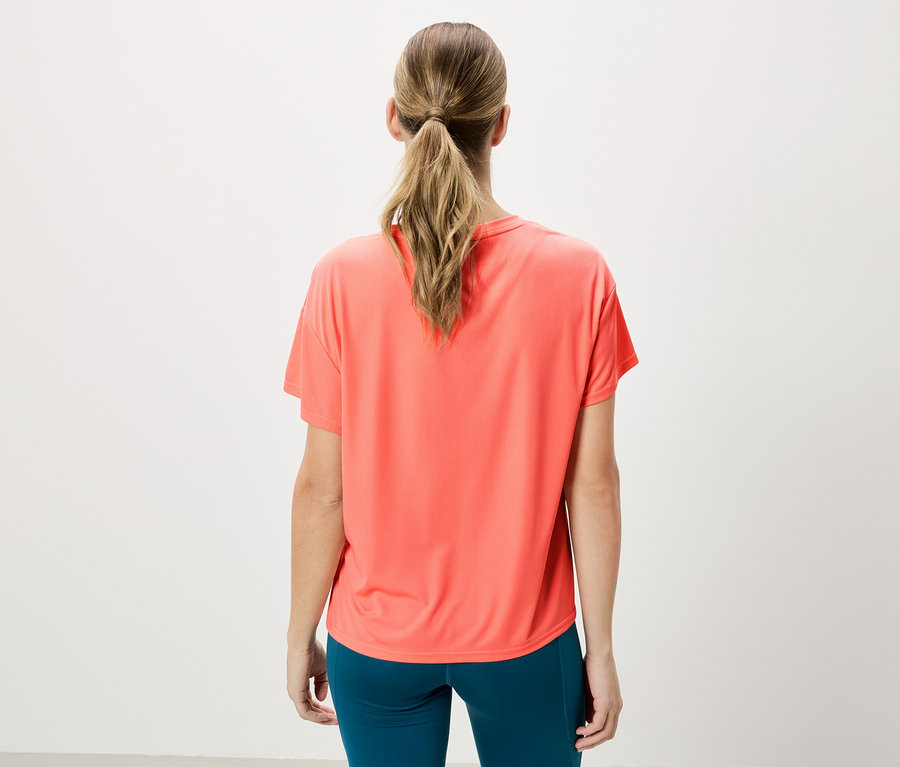 Femme vue de dos, portant un t-shirt corail et des leggings bleus sur un fond blanc.