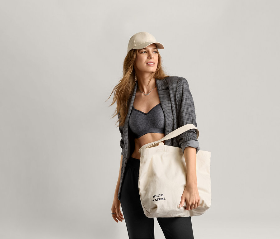 Une femme portant un soutien-gorge de sport, un blazer et une casquette tient un sac fourre-tout.