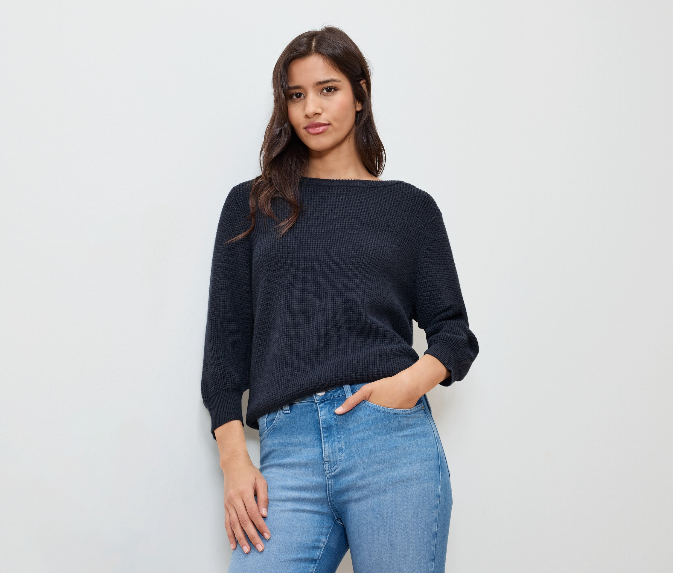 Femme avec une main dans sa poche, portant un pull en maille fine bleu foncé.