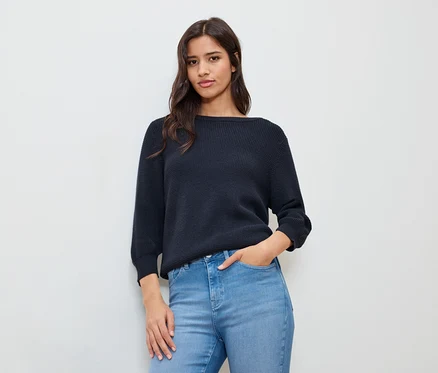 Femme avec une main dans sa poche, portant un pull en maille fine bleu foncé.