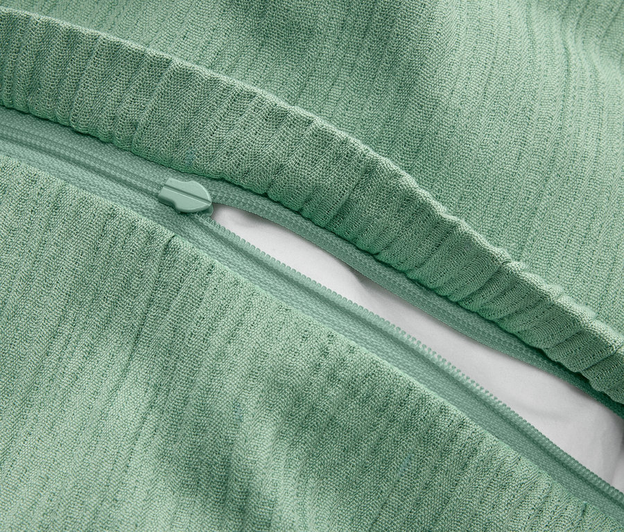 Gros plan d'une taie d'oreiller vert clair avec une fermeture éclair partiellement ouverte, laissant apparaître l'oreiller blanc en dessous.