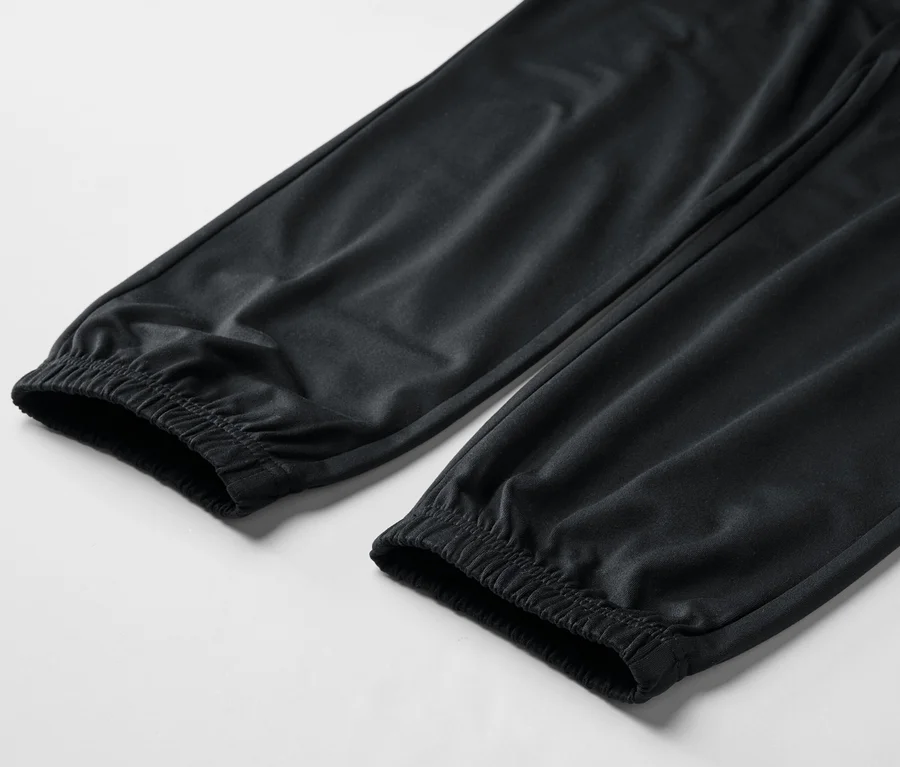 Gros plan sur deux jambes de pantalon noir avec des poignets élastiques sur fond blanc.