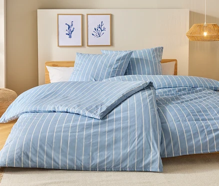 Lit avec des draps rayés bleu et blanc, deux oreillers et deux tableaux au mur.