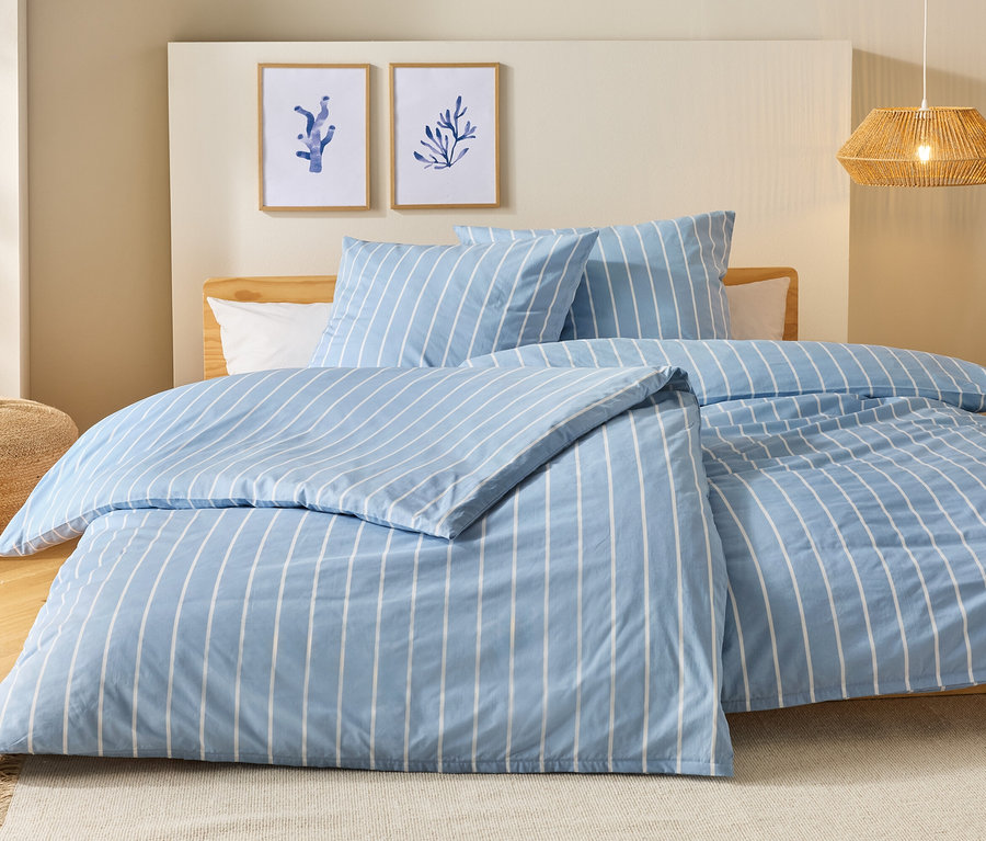 Lit avec des draps rayés bleu et blanc, deux oreillers et deux tableaux au mur.