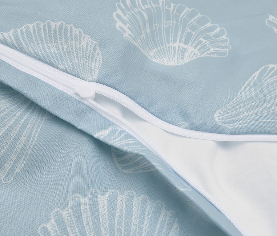Gros plan d'une housse de couette bleu clair avec un motif de coquillages blancs et une fermeture éclair blanche partiellement ouverte.