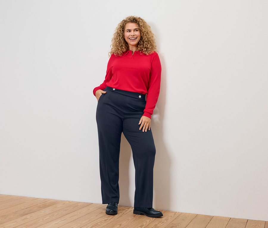 Femme aux cheveux bouclés, haut rouge et pantalon bleu.
