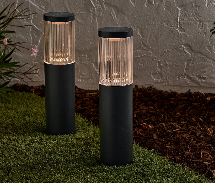 Deux lampes solaires noires se dressent sur une pelouse devant un mur.