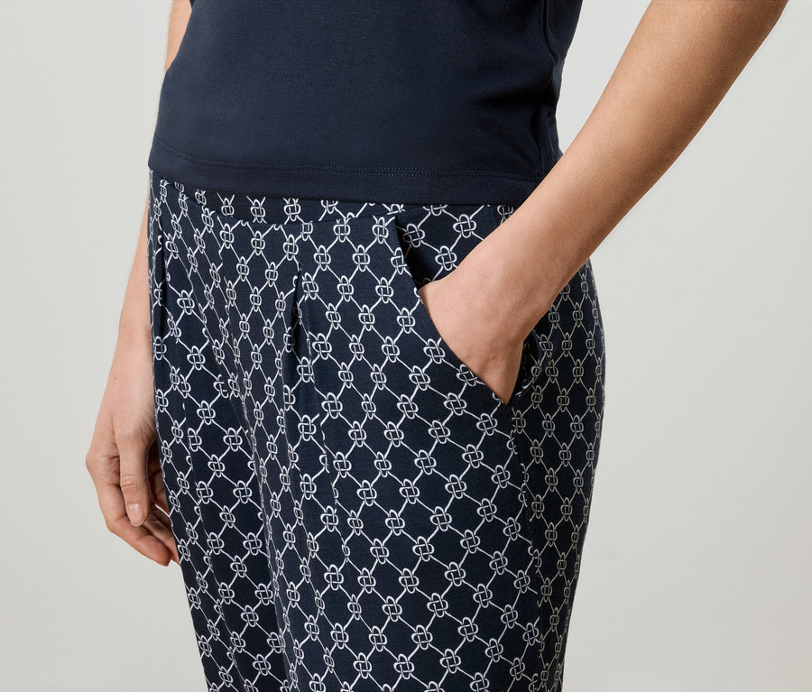Gros plan d'une femme portant un pantalon à motifs bleu marine et un haut bleu marine, avec sa main dans sa poche.