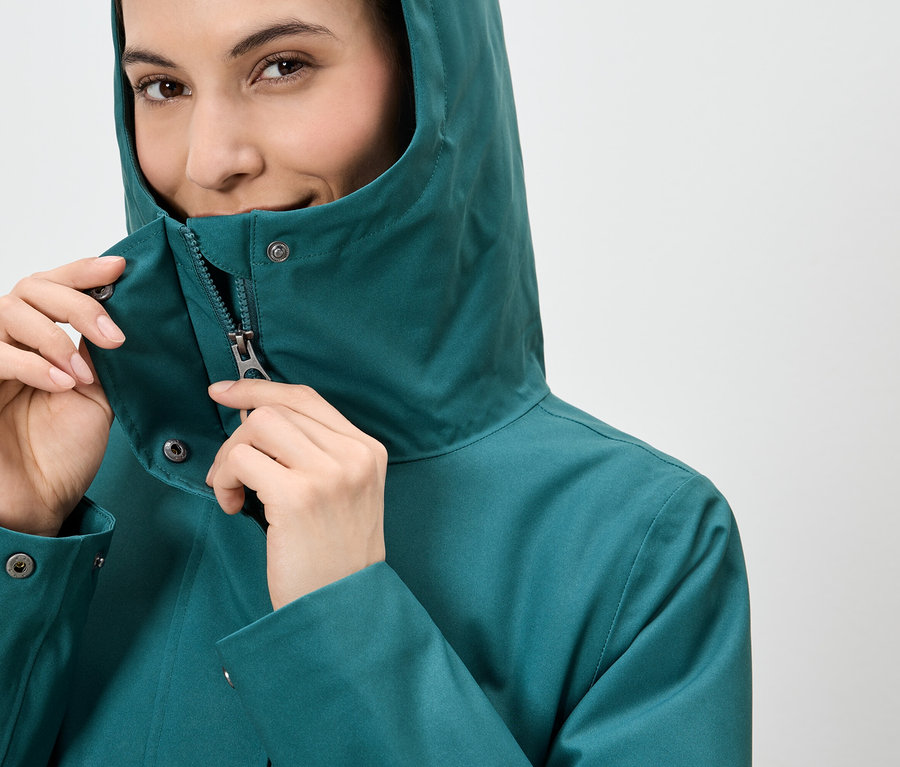 Femme fermant la fermeture éclair d'un imperméable vert émeraude à capuche.