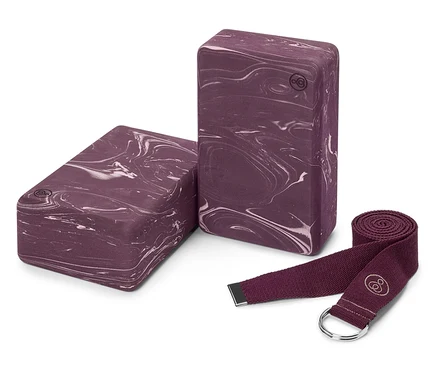 Deux blocs de yoga aubergine marbrés et une sangle de yoga aubergine sont posés sur un fond blanc.