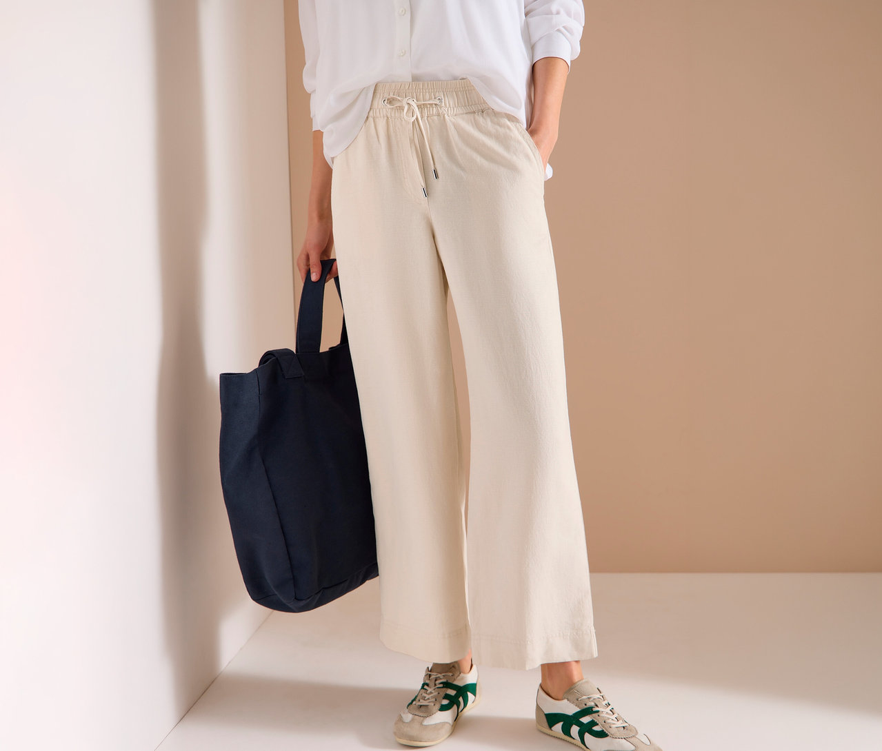 Femme portant un pantalon beige, une chemise blanche, des baskets et un sac fourre-tout bleu.