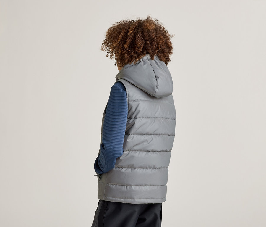 Vue arrière d'une personne aux cheveux bouclés portant un gilet gris matelassé à capuche sur un haut bleu et un pantalon foncé.