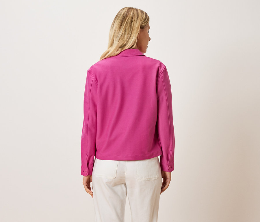Vue arrière d'une femme blonde portant une veste rose et un pantalon clair.