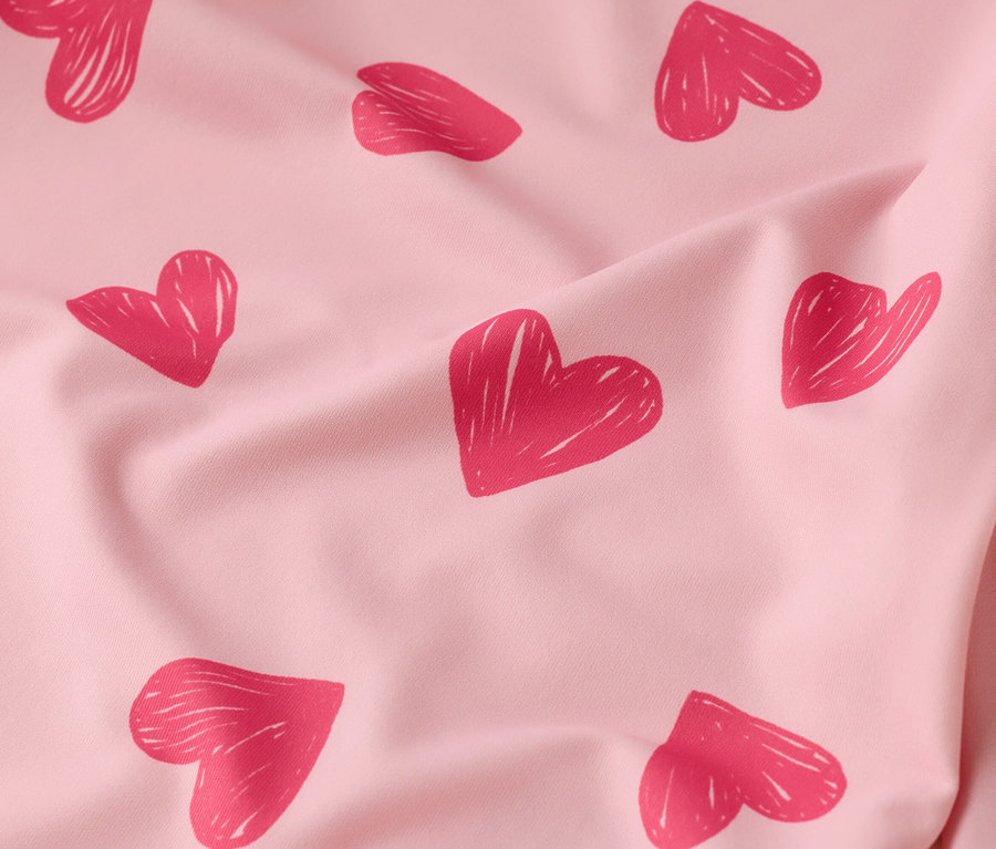 Gros plan d'un tissu rose clair froissé avec des motifs de cœurs rouges.