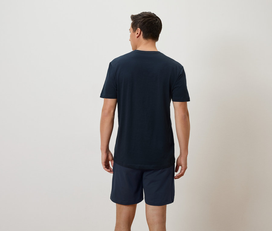 Homme vu de dos portant un t-shirt bleu marine et un short sur un fond neutre.