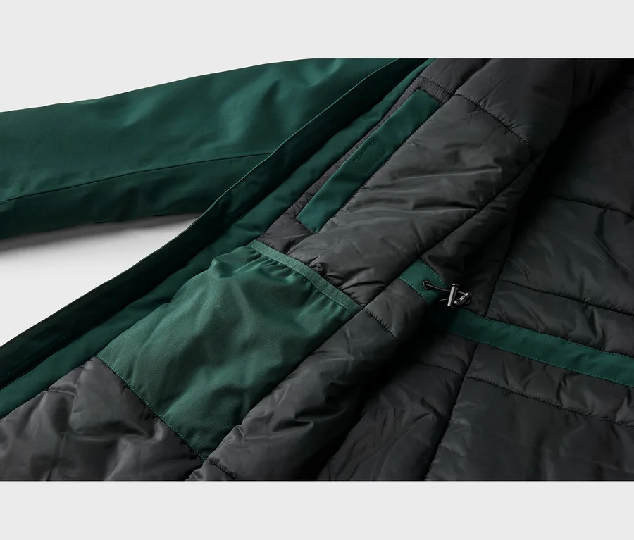 Gros plan de l'intérieur d'une veste vert foncé, montrant sa doublure matelassée noire, une poche intérieure vert foncé et un cordon de serrage avec un stoppeur.