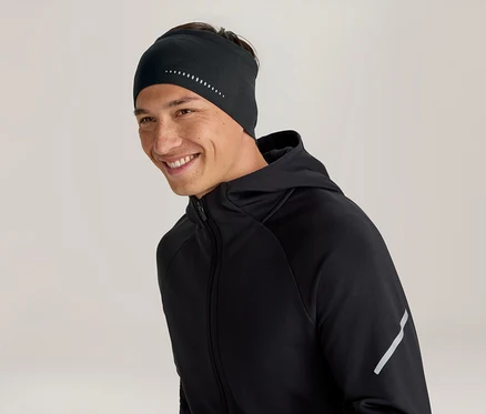 Homme souriant portant un bandeau noir à pois réfléchissants et une veste à capuche noire avec une bande réfléchissante sur la manche.